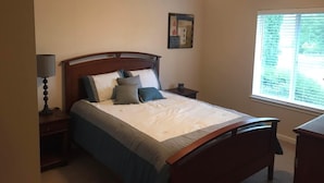 A bedroom with a bed, bedside tables, a lamp, a window, and a painting on the wall.
