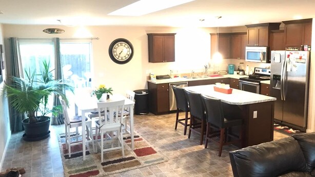 A modern kitchen with a central island, dark wooden cabinets, a stainless steel refrigerator, and a dining area with a table and chairs.