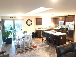 Una cocina moderna con una isla central, armarios de madera oscura, un refrigerador de acero inoxidable y un comedor con mesa y sillas.