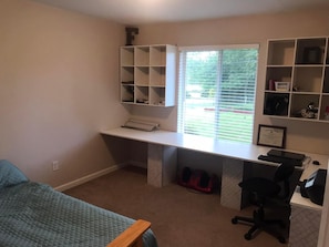 Cozy bedroom with a single bed, desk, and shelving unit, offering a view of the outdoors.