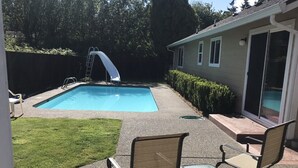 A backyard with a swimming pool, a slide, and a patio area with chairs.