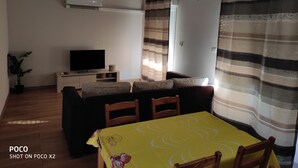 A living room with a sofa, a TV, a dining table with chairs, and yellow pendant lights. - Renovated apartment (Marseille)