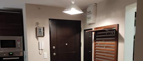 A room with a dark wooden door, a built-in microwave, a small refrigerator, and a wooden bench.