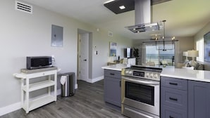 A modern kitchen with grey cabinets, a stainless steel stove, and a microwave on a white countertop. - Spectacular Direct Oceanfront Condo ~ Wraparound Balcony  ~ Top Floor! (Saint Augustine)