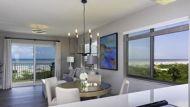 A modern hotel room with a balcony, a round dining table, and a large window with a view of the beach. - Spectacular Direct Oceanfront Condo ~ Wraparound Balcony  ~ Top Floor! (Saint Augustine)