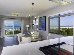Una habitación de hotel moderna con balcón, una mesa de comedor redonda y un ventanal con vista a la playa.