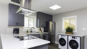 A modern kitchen with grey cabinets, a stainless steel refrigerator, a built-in washing machine, and a large island with a sink. - Spectacular Direct Oceanfront Condo ~ Wraparound Balcony  ~ Top Floor! (Saint Augustine)