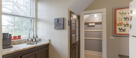 A kitchen with a window, a sink, cabinets, and a door leading to a pantry.