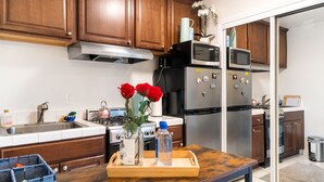 A kitchen with wooden cabinets, stainless steel appliances, and a wooden table with a tray holding a vase of red roses and a water bottle. - Cozy Studio - Mins to WeWork, Sony Pics & Venice with Parking (Culver City)