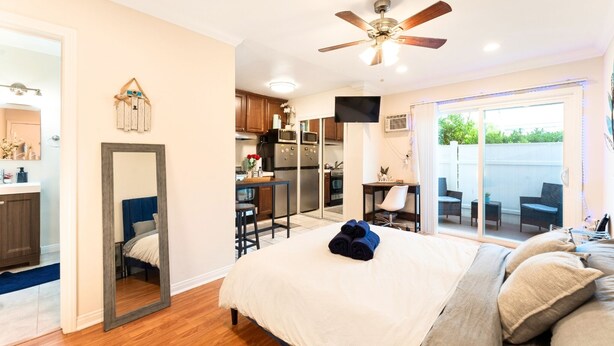A bedroom with a large bed, a ceiling fan, a TV, and a sliding glass door leading to a patio. - Cozy Studio - Mins to WeWork, Sony Pics & Venice with Parking (Culver City)