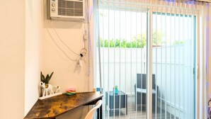 A room with a wooden desk, a white chair, a potted plant, and a view through a sliding glass door to an outdoor area with a table and chairs. - Cozy Studio - Mins to WeWork, Sony Pics & Venice with Parking (Culver City)