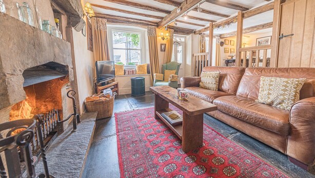 A cozy living room with a fireplace, leather sofa, and a patterned rug. - Bowmanstead Cottage - quirky & cosy traditional village cottage (Coniston)