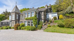A large, stone house with multiple windows and a prominent tower. - Drawing Room, grand apartment with stunning lake views across Beatrix Potter country (Far Sawrey)
