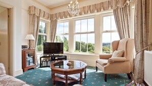 A living room with a television, a sofa, a chair, a coffee table, and a bookshelf. - Drawing Room, grand apartment with stunning lake views across Beatrix Potter country (Far Sawrey)