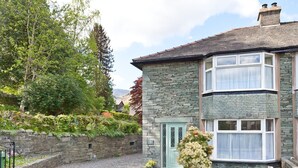 A stone building with a green door, a gravel driveway, and a garden with various plants. - Green Croft - garden cottage in Coniston village (CONISTON)