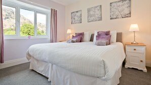 A bedroom with a large bed, two bedside lamps, a nightstand, and three wall-mounted artworks. - Green Croft - garden cottage in Coniston village (CONISTON)