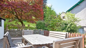 A wooden outdoor seating area with a table and benches, surrounded by a stone wall and a wooden fence. - Green Croft - garden cottage in Coniston village (CONISTON)