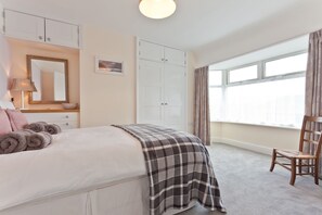 Une chambre à coucher avec un lit, une chaise, une armoire, un miroir et une fenêtre.