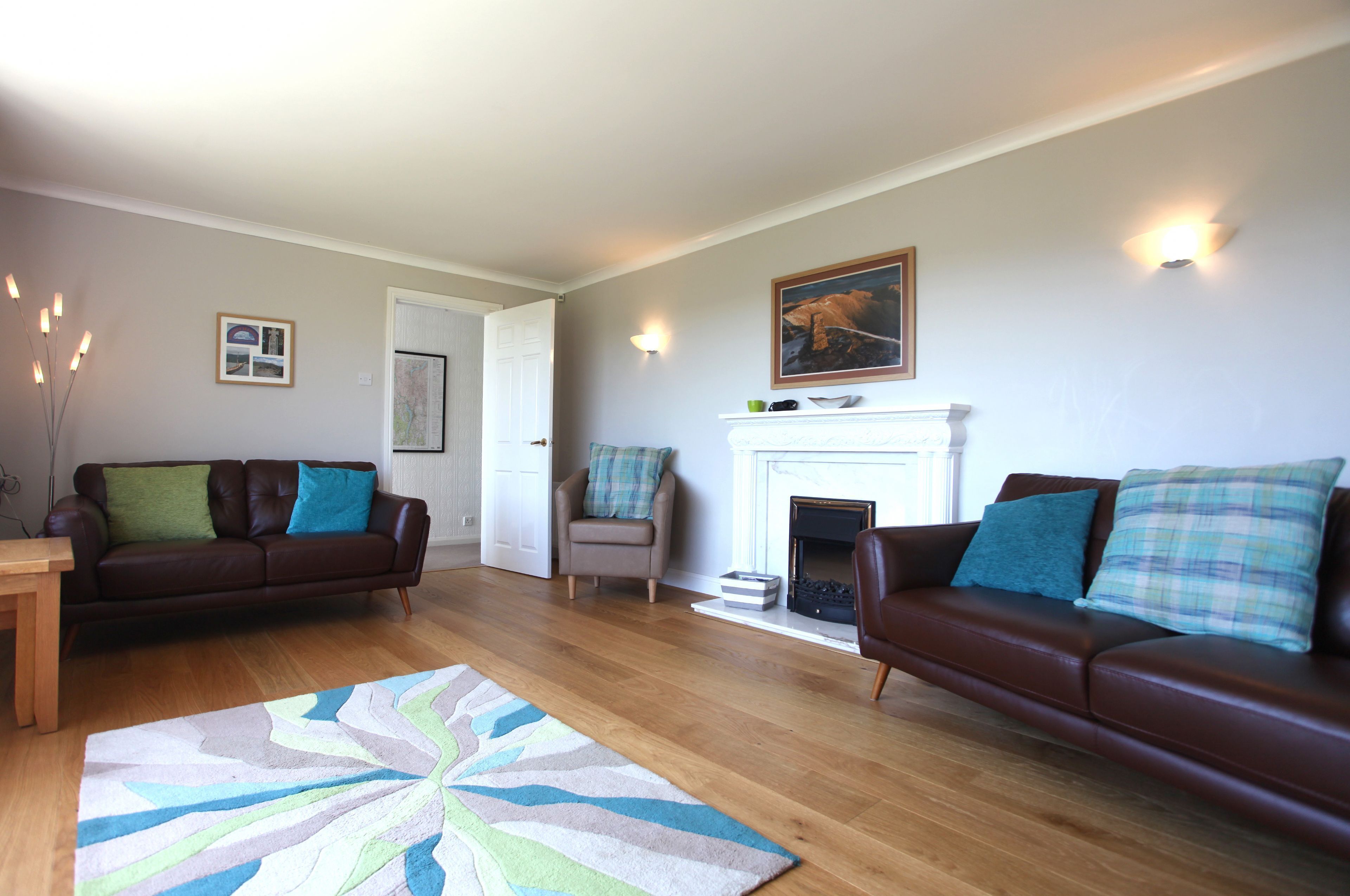 A living room with two brown leather sofas, a wooden coffee table, a patterned rug, a fireplace, and wall-mounted lighting.