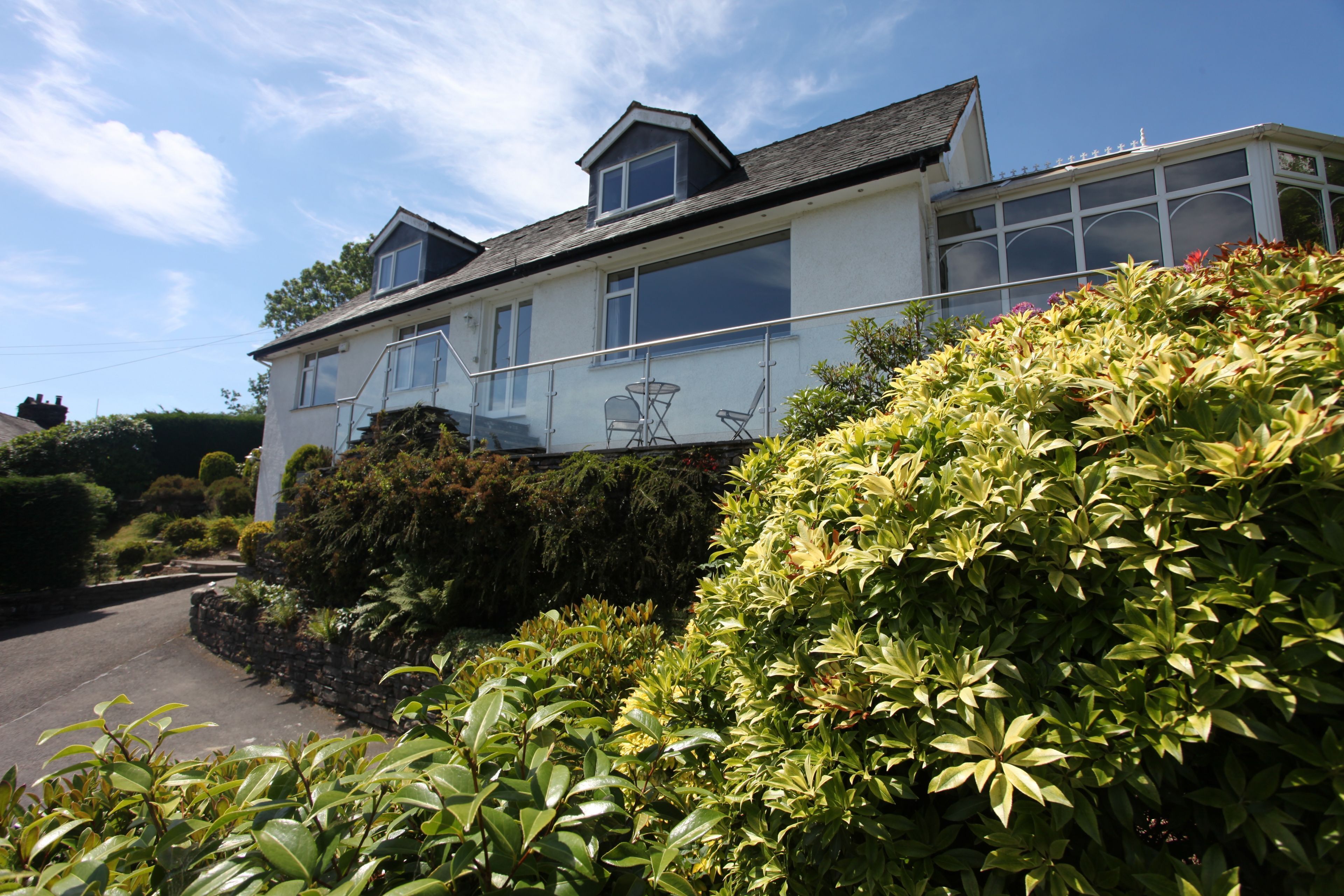A two-story house with a balcony, surrounded by lush greenery.