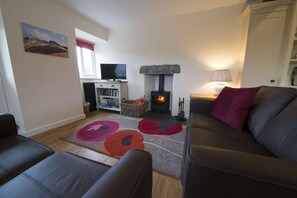 A living room with a fireplace, a sofa, a TV, and a bookshelf. - Poppy Cottage, village cottage with lake views (Coniston)