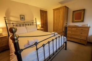 A neatly made bed with a metal frame, wooden wardrobe, and a bedside table with a lamp. - Poppy Cottage, village cottage with lake views (Coniston)