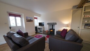 A cozy living room with two leather sofas, a fireplace, and a television. - Poppy Cottage, village cottage with lake views (Coniston)
