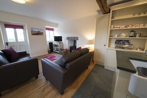 A living room with two sofas, a television, and a fireplace. There is a kitchen area with a coffee maker and a kettle. - Poppy Cottage, village cottage with lake views (Coniston)