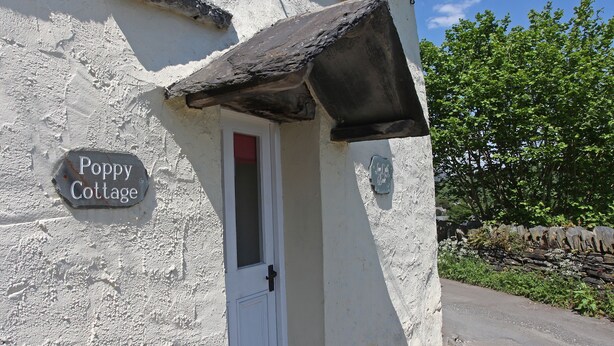 A cottage with a white exterior, a stone wall, and a sign reading "Poppy Cottage." - Poppy Cottage, village cottage with lake views (Coniston)