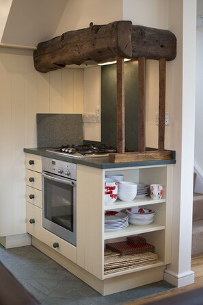 A compact kitchen with a built-in oven, a stovetop, and a wooden beam overhead. - Poppy Cottage, village cottage with lake views (Coniston)