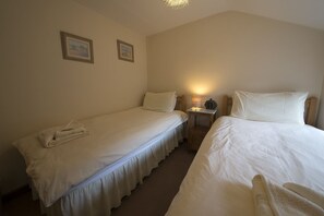 A twin room with two single beds, a bedside table with a lamp, and two framed pictures on the wall. - Poppy Cottage, village cottage with lake views (Coniston)