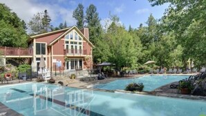 A two-story building with a pool area, including a smaller pool and a larger pool, surrounded by trees. - Elegant 4BR Condo for 8 • Ski Views • Walk to Village • Spa & Shuttle (Mont-Tremblant)
