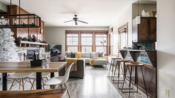 A modern kitchen with wooden cabinets, a dining area with a wooden table and chairs, and a cozy living space with a sofa and a ceiling fan. - Elegant 4BR Condo for 8 • Ski Views • Walk to Village • Spa & Shuttle (Mont-Tremblant)