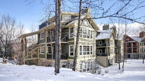 A multi-story building with a stone facade, multiple balconies, and a staircase leading to the entrance. - Elegant 4BR Condo for 8 • Ski Views • Walk to Village • Spa & Shuttle (Mont-Tremblant)