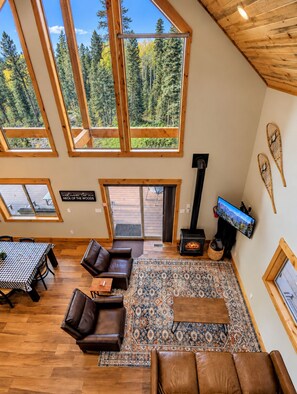 A spacious living room with high ceilings, large windows, a fireplace, and a television.