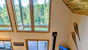 Ein geräumiges Wohnzimmer mit Kamin, Fernseher und Blick ins Freie durch große Fenster.