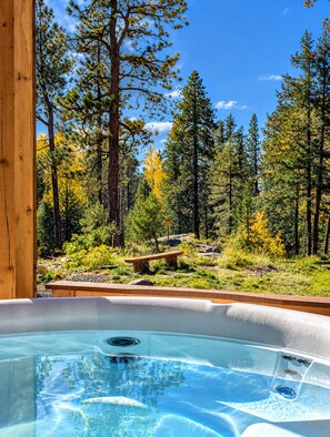 A hot tub in a forested area with a wooden deck and a bench.