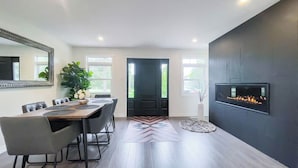 A modern dining area with a black door, a fireplace, and a large mirror. - Huron Time - King bed! (Bayfield)
