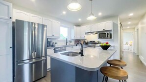 A modern kitchen with stainless steel appliances, white cabinetry, and a central island with stools. - Huron Time - King bed! (Bayfield)