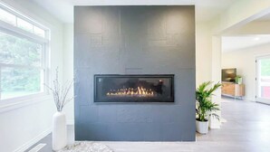 A modern living room with a built-in fireplace, large windows, and a minimalist design. - Huron Time - King bed! (Bayfield)
