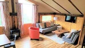 Una habitación acogedora con un sofá, una silla roja, una mesa de madera y un televisor fijado a la pared.