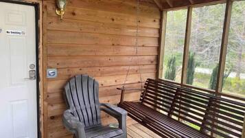 A wooden cabin with a porch, a bench, a chair, and a door with a 'No Smoking' sign.