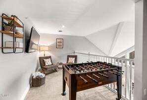 Un acogedor dormitorio tipo loft con mesa de fútbol, una silla cómoda, una lámpara y una estantería.