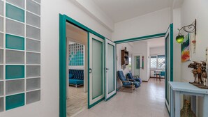 Un couloir avec des portes encadrées de motifs turquoise, qui donnent sur un espace de vie comprenant un canapé et des fauteuils.