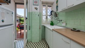 Une cuisine avec des carreaux de céramique verts, un sol à carreaux, un plan de travail en bois et une fenêtre donnant sur l’extérieur.