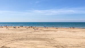 Une vaste plage de sable où l’on voit des gens et des parasols, un ciel dégagé et une mer calme.
