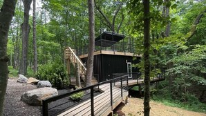 A wooden deck with a metal railing, surrounded by large rocks and hydrangea bushes. - The Oaklyn Container ~ Hocking Hills ~ Hot tub ~ Firepit ~ Wifi (Logan)