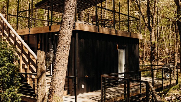 A wooden cabin with a staircase leading to a covered entrance, surrounded by trees. - The Oaklyn Container ~ Hocking Hills ~ Hot tub ~ Firepit ~ Wifi (Logan)
