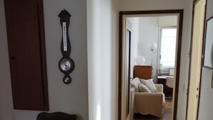 Un couloir étroit avec une chaise, une horloge murale et une porte donnant sur une autre pièce.
