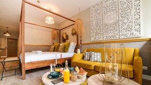 A modern bedroom with a wooden four-poster bed, a yellow sofa, a breakfast table with breakfast items, and decorative wall art. - The Majestic Garden Suite (Paris)